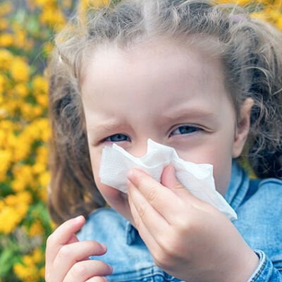 Flicka med pollenallergi som snyter sig.